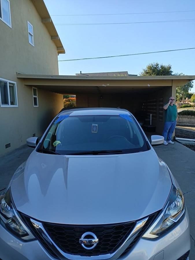 Nissan Sentra in a carport with a fresh windshield still taped at the edges